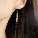 Gold chain earring worn by a person with long dark hair.